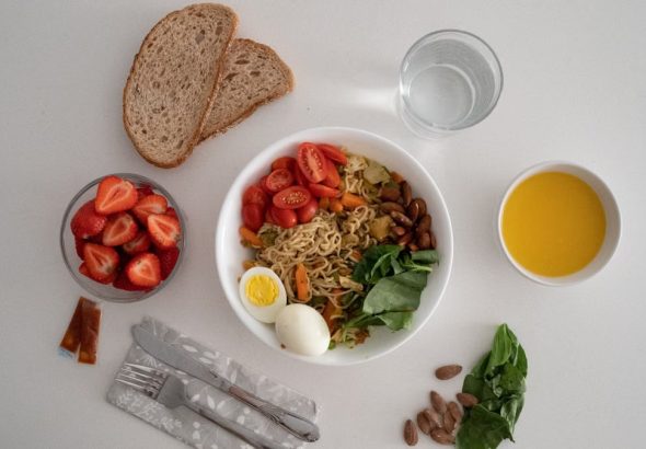 A balanced meal featuring a variety of healthy ingredients including noodles, eggs, almonds, strawberries, and fresh vegetables.